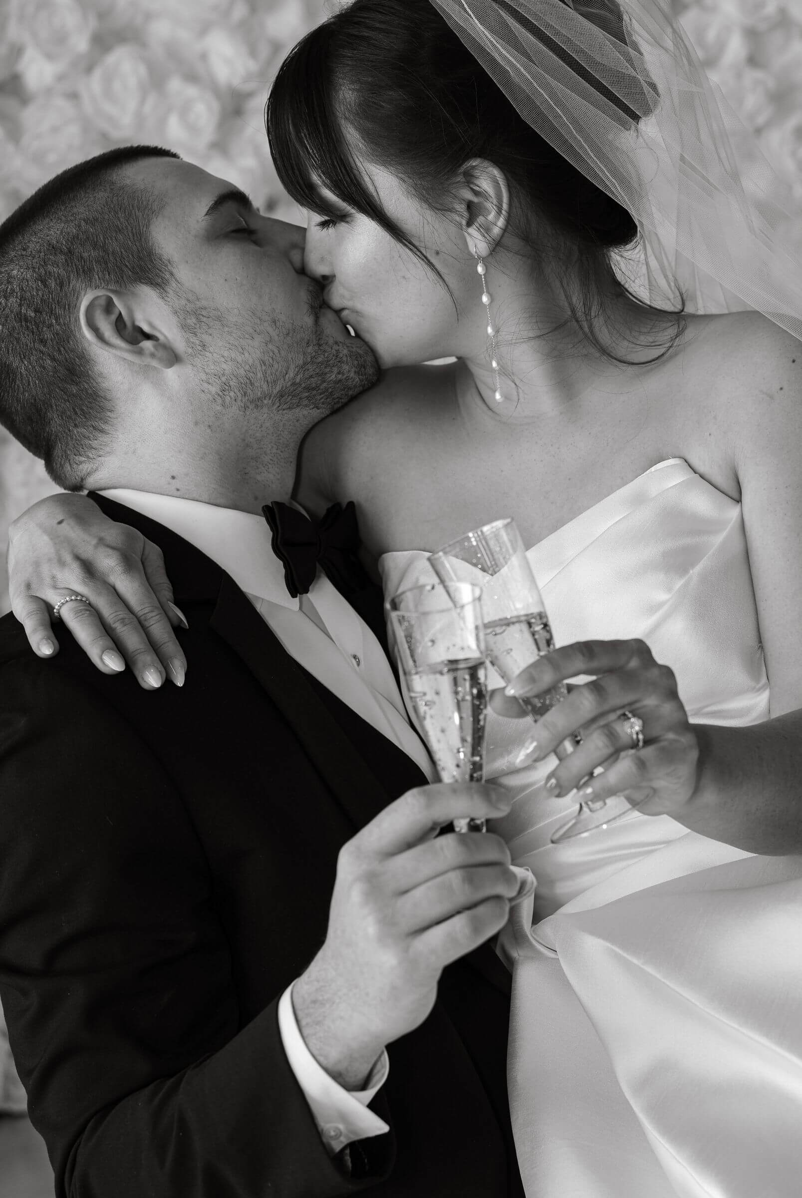 Bride and groom kiss with champagne at Pinter's Event Center, dressed in wedding attire.